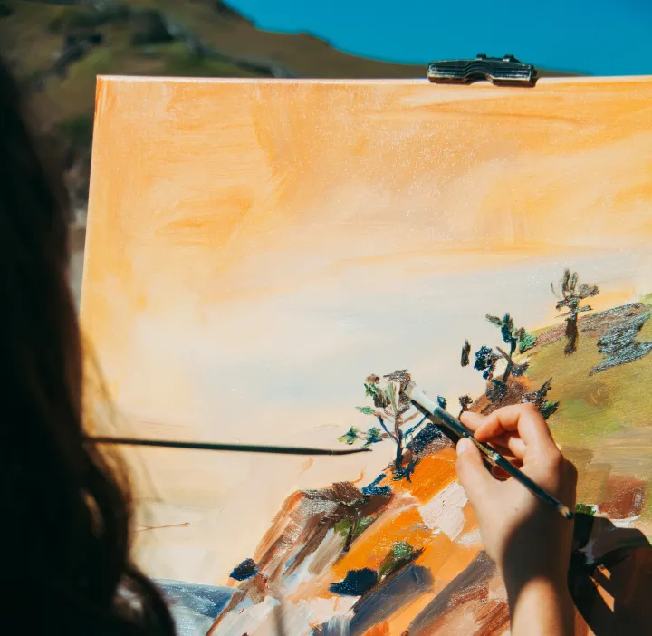 A painter at an easel outdoors, brush touching a half-finished landscape